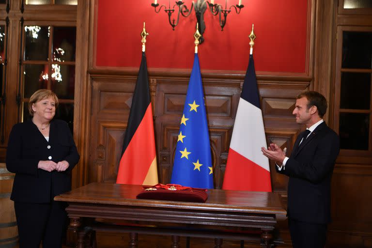 La canciller alemana, Angela Merkel, reacciona mientras el presidente francés, Emmanuel Macron, aplaude mientras recibe la Gran Cruz de la Legión de Honor, en Beaune, Borgoña, el miércoles 3 de noviembre de 2021.