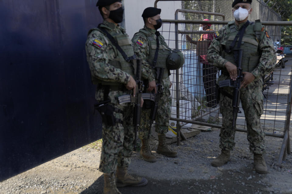 A resident looks through a gate surrounding the Litoral Penitentiary as security forces stand guard after deadly fights inside the jail in Guayaquil, Ecuador, Thursday, July 22, 2021. Rival gangs of inmates fought in two prisons in Ecuador, killing at least 18 people and injuring dozens, authorities said Thursday. (AP Photo/Dolores Ochoa)