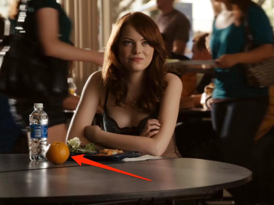 A red arrow pointing to an orange at a cafeteria table in "Easy A."