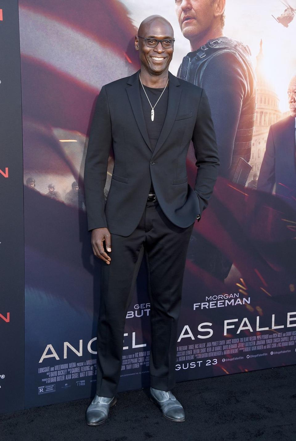 lance reddick, wearing a black suit, standing in front of an angel has fallen poster