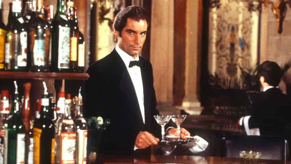 Timothy Dalton in a tuxedo holding a tray of martinis