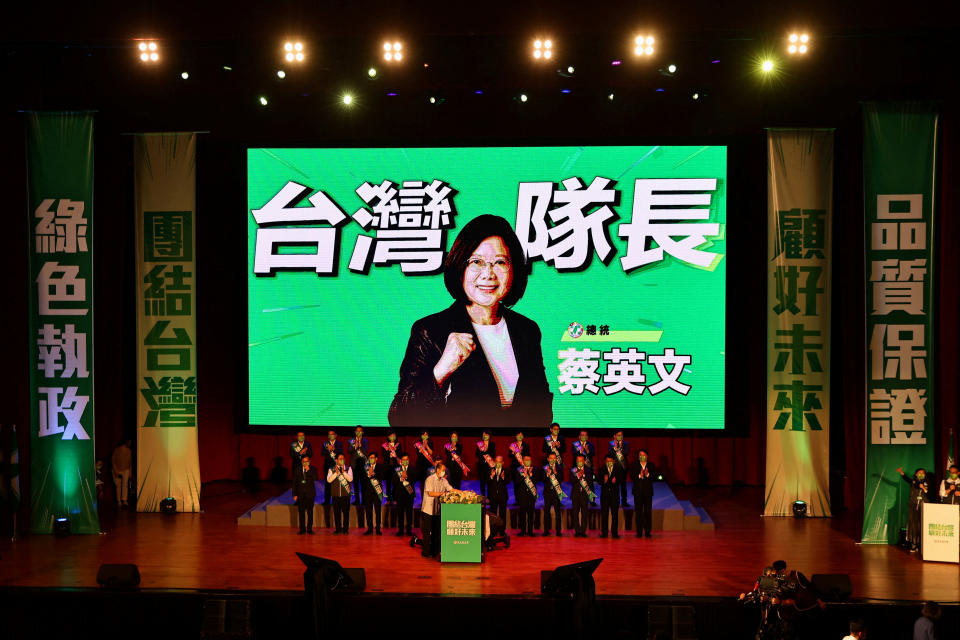 A few dozen people stand on stage in front of a large screen with an image of Taiwan President Tsai Ing-wen.