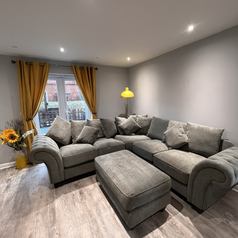 A living room with a large sectional couch, hardwood floors and glass doors that lead to an outdoor area