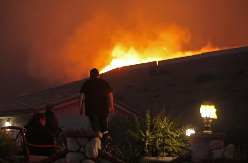 A homeowner watches flames burn a hillside near Foxtail Drive and Lotus Avenue in Yorba Linda.