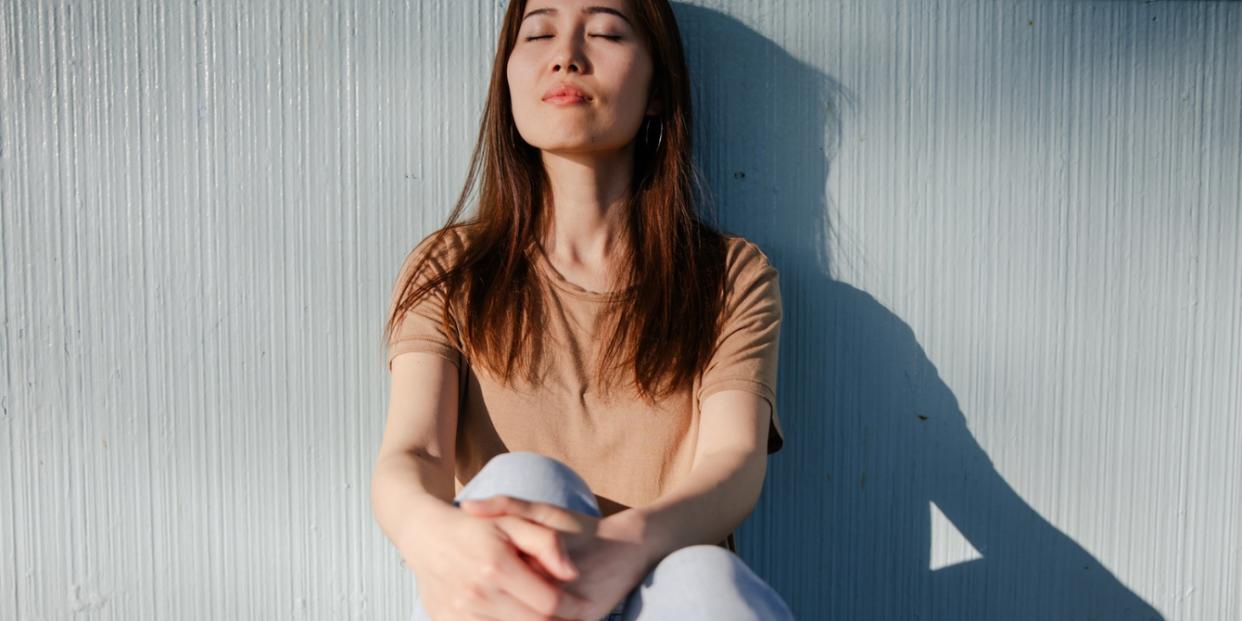 woman with eyes close leaning on wall