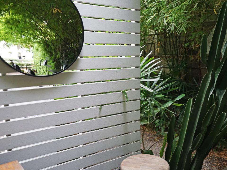 gray paneled fence with circular mirror surrounded by greenery