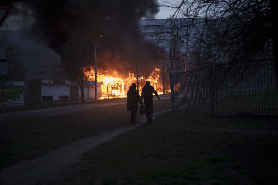 A couple of residents walk past burning shops after a Russian attack in Kharkiv, Ukraine, Monday, April 11, 2022. (AP Photo/Felipe Dana)