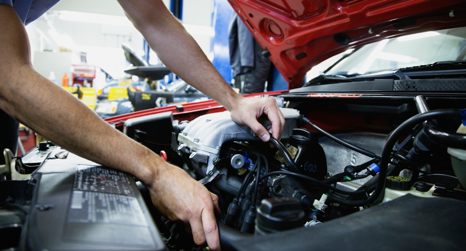 A mechanic works under the bonnet of a car. 