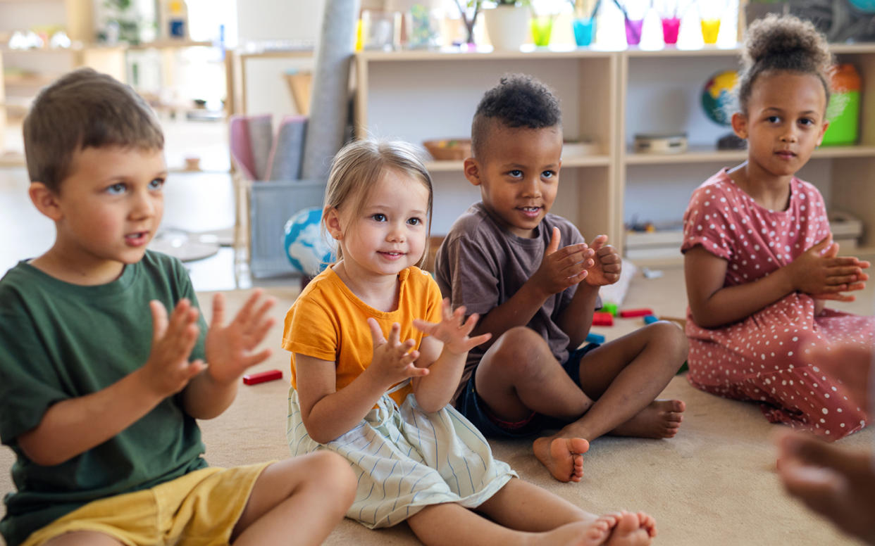 Group of small nursery school children sitting on floor indoors in classroom, clapping