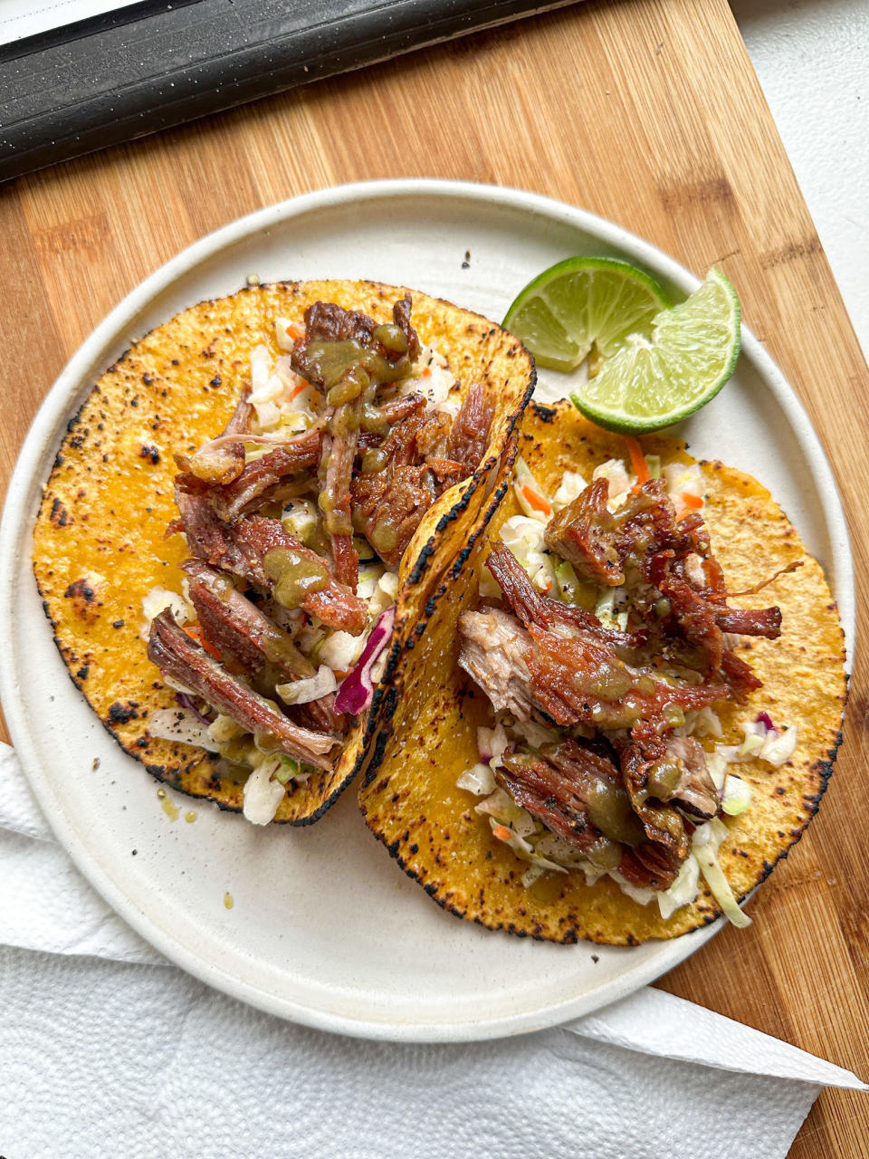 plated carnitas tacos with slaw, hot sauce, and lime wedges next to the plate, for squeezing