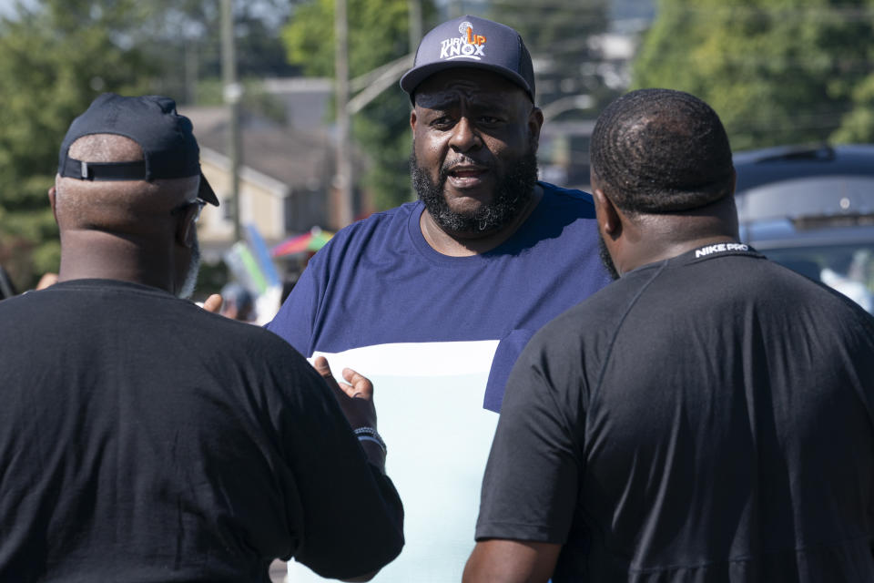 Kodi Mills, center, of Turn Up Knox talks with people enjoying the Lonsdale Neighborhood Homecoming celebration Saturday, Aug. 5, 2023 in Knoxville, Tenn. The organization is the centerpiece of Knoxville's attempt to follow a science-based playbook to fight a surge in fatal and non-fatal shootings. (AP Photo/George Walker IV)