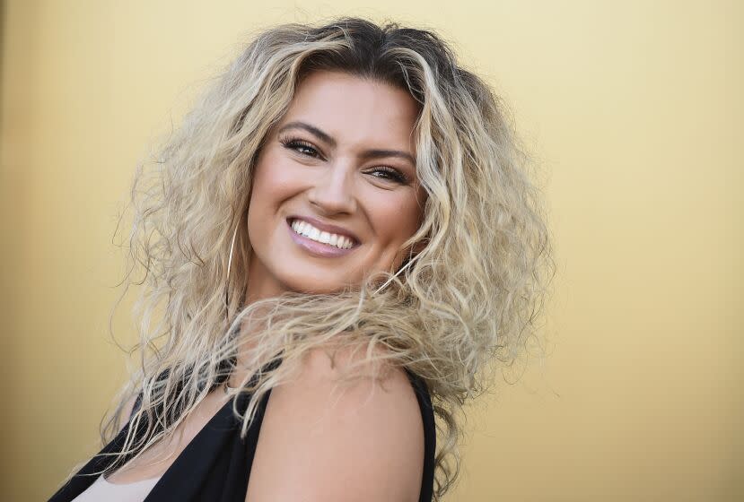 Tori Kelly smiling in a black-and-white outfit against a yellow backdrop.