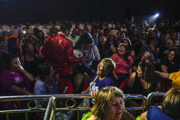 Audience members bust out laughing as Arturo Peña in his role as "La loca de la cartera", or “The Crazy Purse Lady,” engages with the public during a Timoteo Circus show, on the outskirts of Santiago, Chile, Sunday, Dec. 18, 2022. Peña said that during the Augusto Pinochet military dictatorship the male artists who dressed as women used to receive kicks and blows during performances, and the idea of carrying a purse in the act was to use in self-defense. (AP Photo/Esteban Felix)