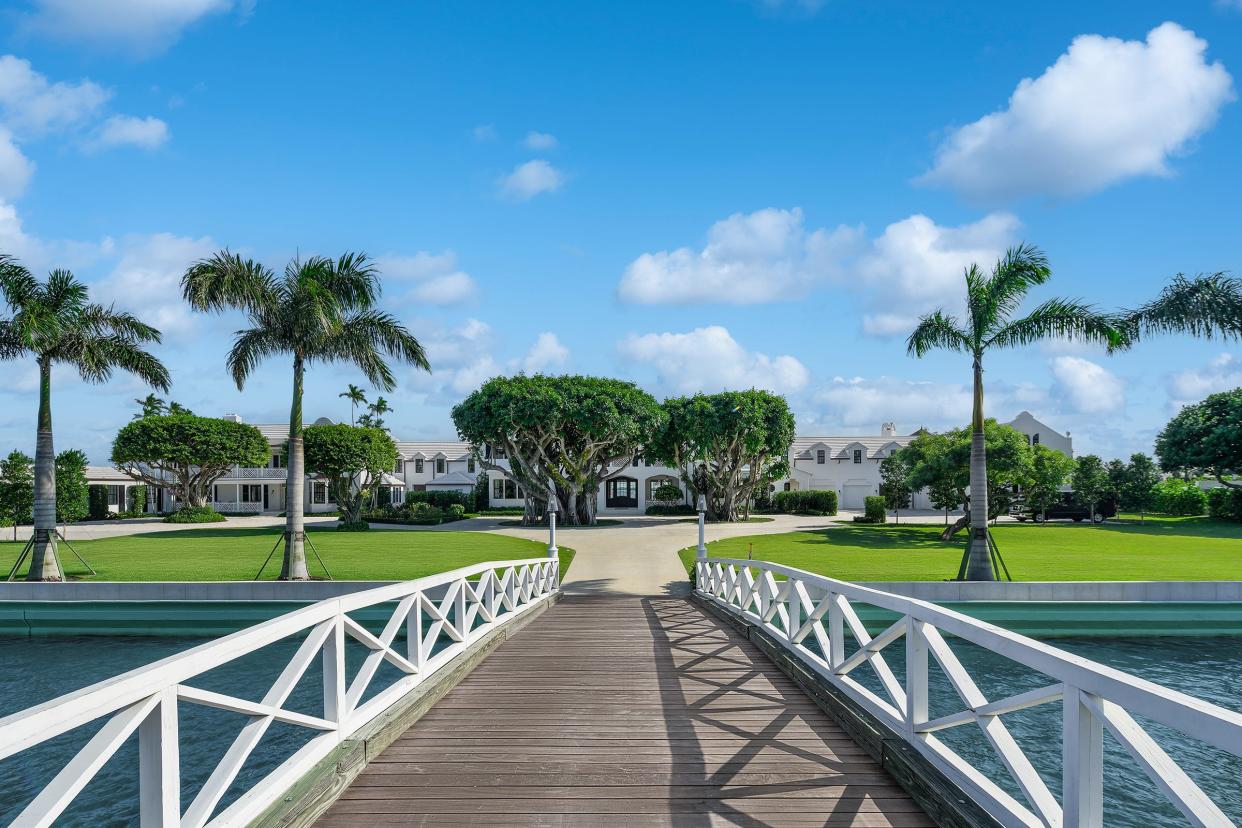 A gated bridge leads onto private Tarpon Island in Palm Beach, where the British Colonial-style house stretches along the waterfront. The property is lined with 29 royal palms.