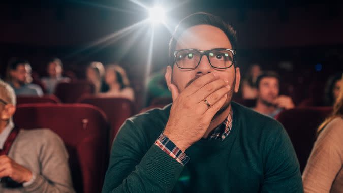 Young man watching a horror movie at the cinema.