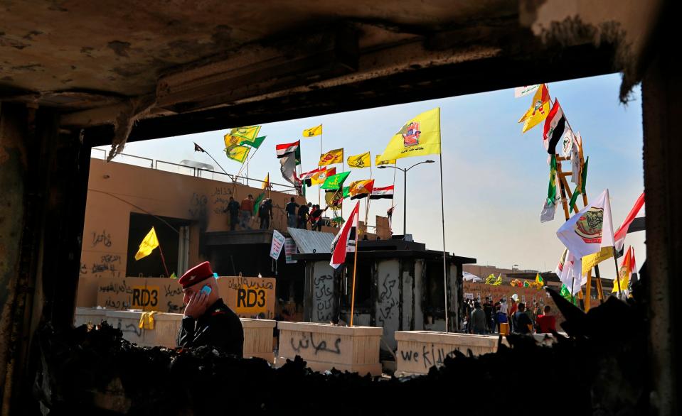 Pro-Iranian militiamen and their supporters are seen through a broken window of a burned checkpoint in front of the U.S. embassy in Baghdad, Iraq, Wednesday, Jan. 1, 2020.