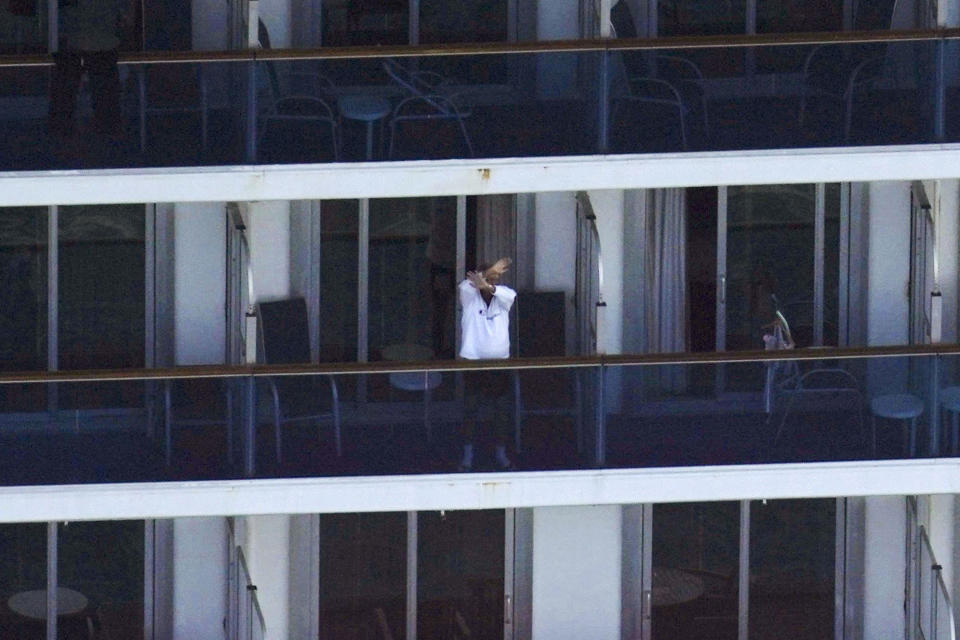 A passenger waves from the cruise ship Diamond Princess anchored off Yokosuka, near Tokyo, Saturday, Feb. 8, 2020. Three more cases were diagnosed Saturday among 3,700 passengers and crew on the quarantined ship. Those aboard remain under 14-day quarantine. (Koki Sengoku/Kyodo News via AP)