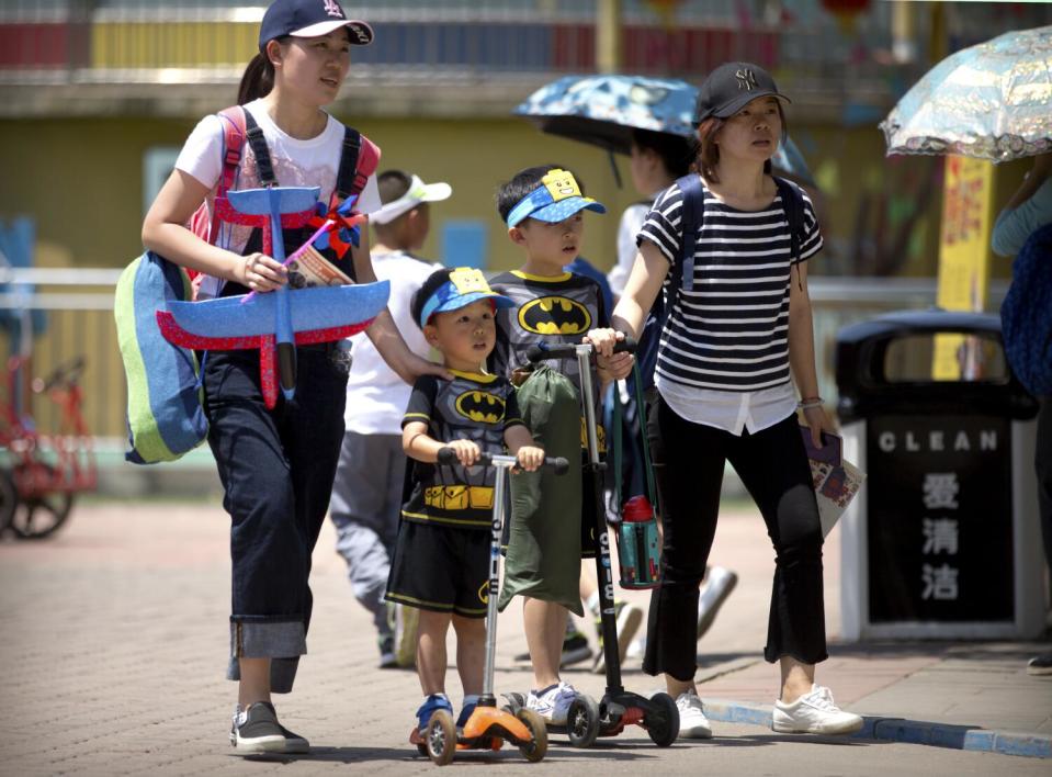 Two women, one carrying toys, walk with children in matching outfits and on scooters at a public park