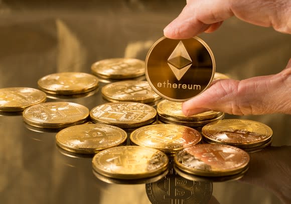 A physical gold Ethereum coin being held up.