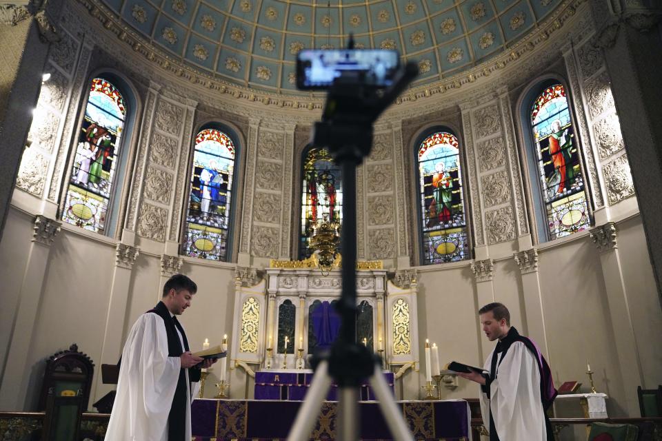 FILE - In this March 29, 2020 file photo, the Rev. Steven Paulikas, right, and curate Spencer Cantrell deliver an Evening Prayer service over Facebook Live in the Brooklyn borough of New York, amid the global COVID-19 coronavirus pandemic. Pastors across the country say they and their congregations have responded with creativity and resiliency — and invigorated community spirit — even as the outbreak forced widespread cancellations of in-person services. (AP Photo/Emily Leshner)