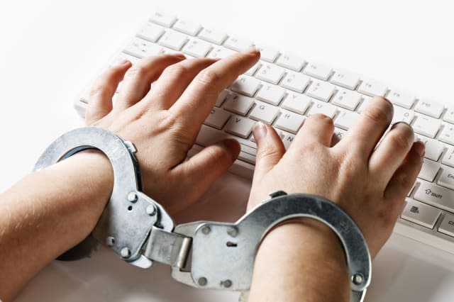 A young woman's hands are locked into handcuffs as she 'slaves away' on a white computer keyboard, against a white background. C