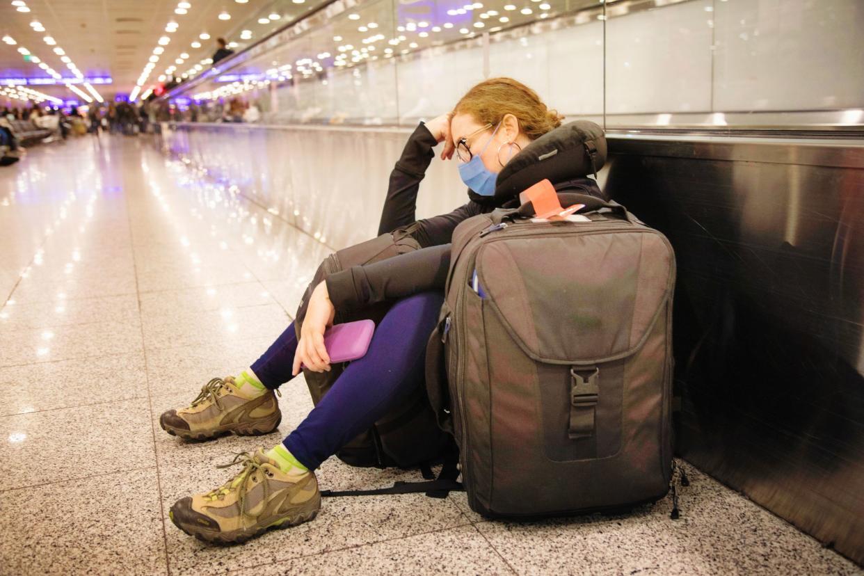 Young Female traveller napping as she waits forever at the airport terminal, wearing a protective mask. She is travelling during covid-19 times.