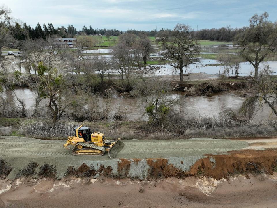 bulldozer drives down dirt road surrounded by flooding