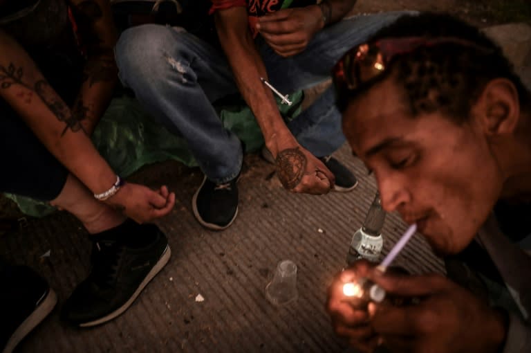Un drogadicto fuma basuco, una droga altamente adictiva que consiste en cocaína de bajo grado mezclada con pasta de coca y otras sustancias, mientras otros se inyectan heroína en el centro de Medellín, Colombia (AFP/JOAQUIN SARMIENTO)