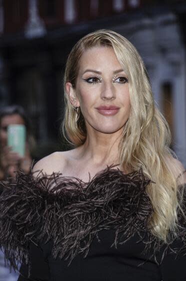 Ellie Goulding smiles in a feather lined black gown with gemstones around her eyes.