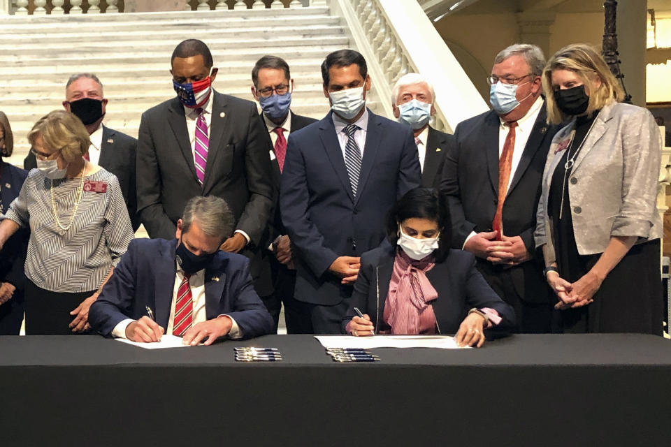 FILE - Georgia Gov. Brian Kemp, left, and Centers for Medicare and Medicaid Services Administrator Seema Verma sign healthcare waivers at the state Capitol in Atlanta, Oct. 15, 2020. Public health advocates say Georgia appears to be doing little to promote its new Medicaid plan or enroll people in it. (AP Photo/Jeff Amy, File)