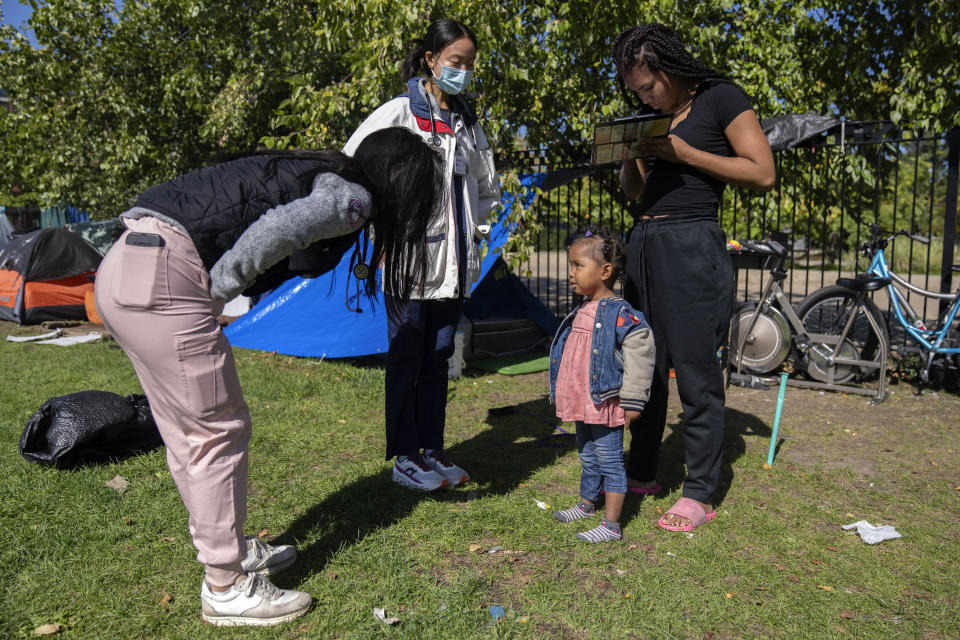 Anmani Rendon of Venezuela, right, fills out paperwork for her 2-year-old daughter Sofia Barragan as med students Christina Guyn, left, and Irene Quan, center, check the girl's health outside of the 12th District police station where migrants are camped, Saturday, Oct. 7, 2023, in Chicago. (AP Photo/Erin Hooley)