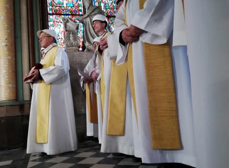 Priests wear hard hats, as the Archbishop of Paris Michel Aupetit leads the first mass in a side chapel two months to the day after a devastating fire engulfed the Notre-Dame de Paris cathedral, in Paris