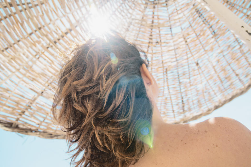 woman and her hair in the back under a white straw umbrella 