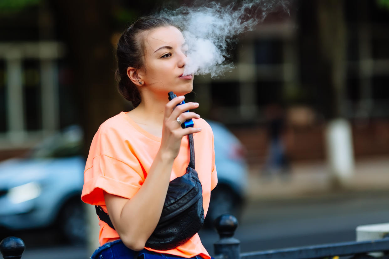 Pretty young girl vape popular ecig gadget,vaping device.Happy brunette vaper girl with e-cig.Portrait of smoker female model with electronic cigarette vaporizer.Ejuice vaping with fruit flavor liquid