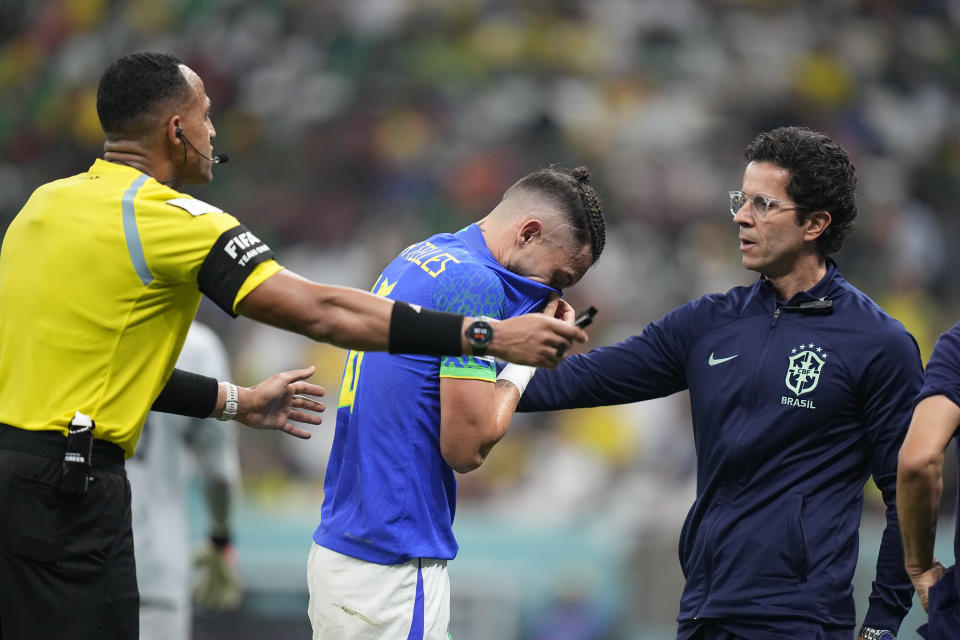 Brazil's Alex Telles, center, uses his shirt to wipe his face as referee Ismail Elfath gestures during the World Cup group G soccer match between Cameroon and Brazil, at the Lusail Stadium in Lusail, Qatar, Friday, Dec. 2, 2022. (AP Photo/Pavel Golovkin)