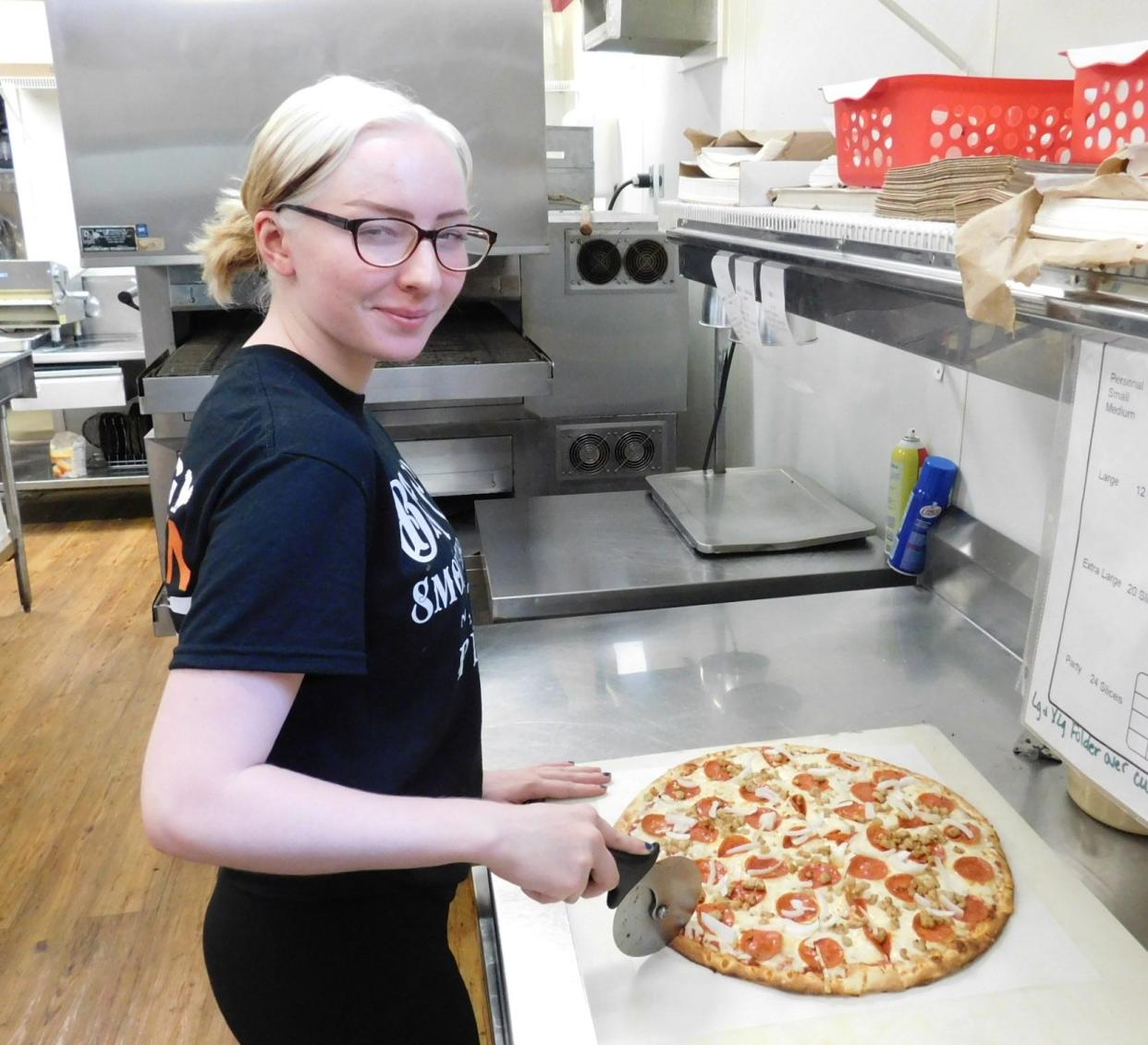 Kaydence Allen slices a pizza in the kitchen at Big C's Smokehouse and Pizza.