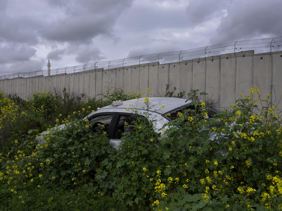 FILE - Bushes grow over an abandoned car next to section of the Israeli separation barrier in the northern Israeli Arab town of Baka Al-Gharbiye, separated from its neighbouring West Bank village of Nazlat Issa, March 9, 2022. (AP Photo/Oded Balilty, File)