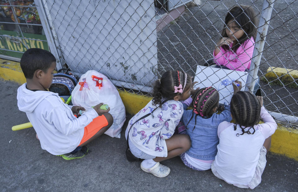 Venezuelan migrant children play with a Costa Rican girl sitting behind a fence in a parking lot, while their parents Richard Plaza and his wife Widner Bijarena clean windshields on one of the streets of San Jose, Costra Rica, Wednesday, Dec. 7, 2022. Faced with an overwhelmed asylum system, Costa Rica, one of the world’s great refuges for those fleeing persecution, is tightening its generous policies after President Rodrigo Chaves said the country’s system is being abused by economic migrants. (AP Photo/Carlos Gonzalez)