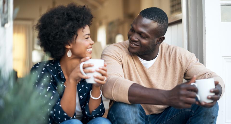 Couple sip from mugs and smile at each other on doorstep. (Getty Images)