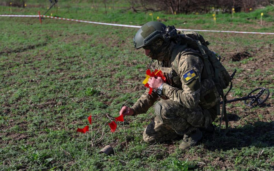 A Ukrainian military sapper places red flags next to a part of a Russian cluster bomb while demining a field