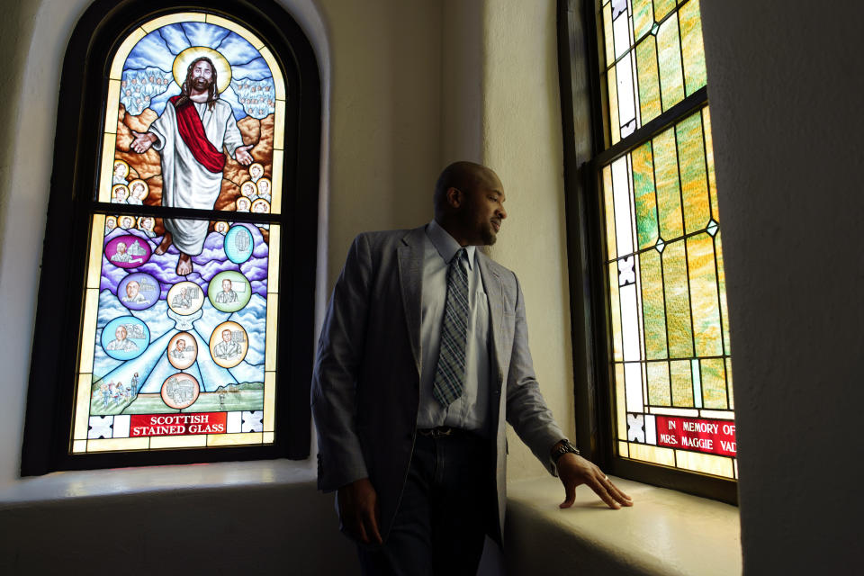 In this May 28, 2021, photo, Rev. Robert R.A. Turner, pastor of the historic Vernon African Methodist Episcopal Church, looks at a stained glass window while giving a tour of the church to a missionary around centennial commemorations of the Tulsa Race Massacre in Tulsa, Okla. Only the basement remained of the church, partially destroyed in the massacre in 1921 that destroyed the area known as Black Wall Street. (AP Photo/John Locher)