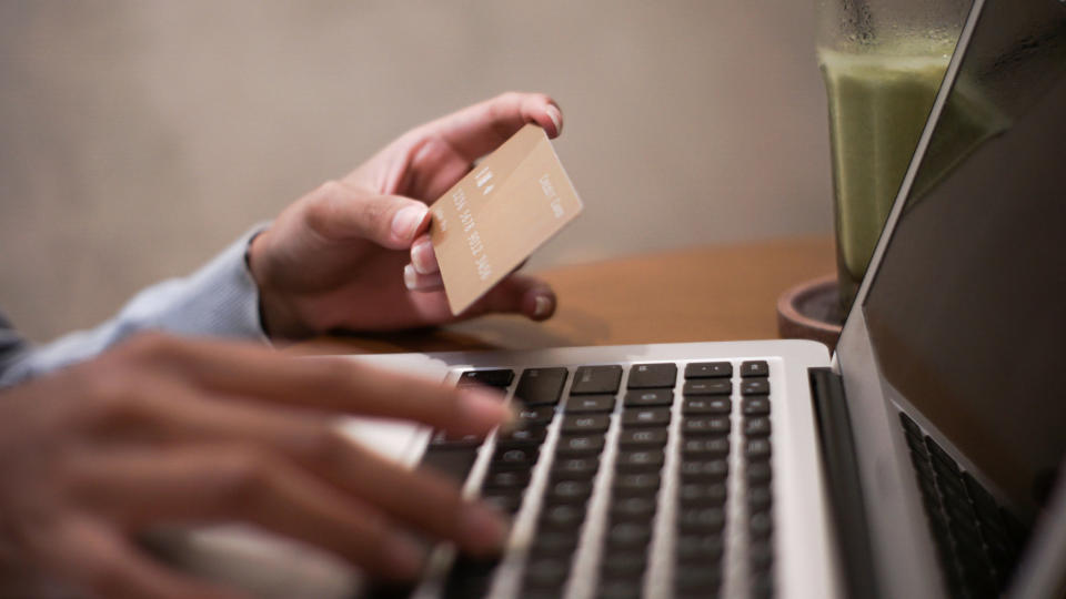 A person typing on a laptop holding a credit card