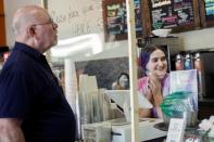 Alyssa Machin serves a customer from behind a plastic shield at SaddleCreek Coffee during the phased reopening from the coronavirus disease (COVID-19) restrictions in Cave Creek