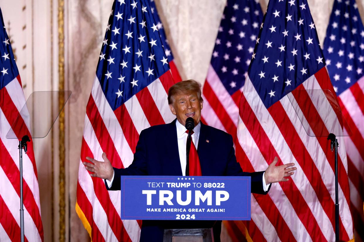 Donald Trump stands with arms wide at the microphone, backed by American flags at a podium saying: Trump Make America Great Again 2024.