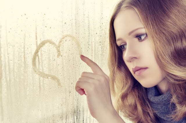 sad enamored girl draws a heart on the window in the rain