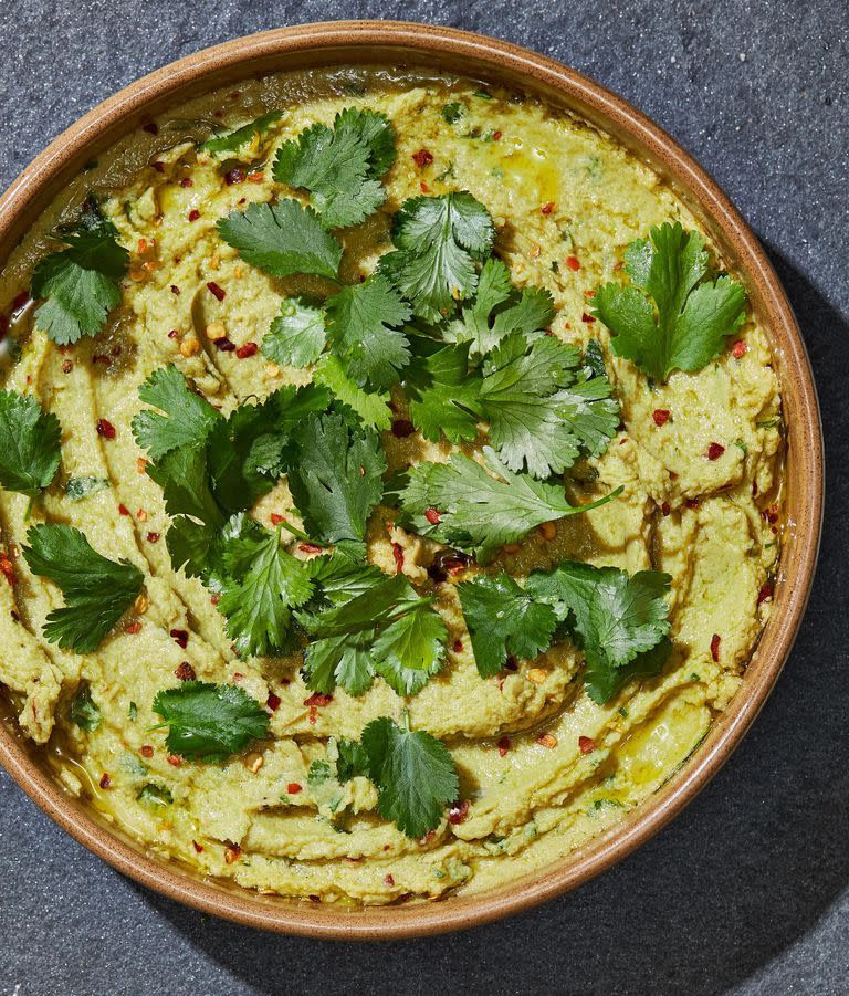 avocado hummus topped with red pepper flakes and cilantro in a brown bowl