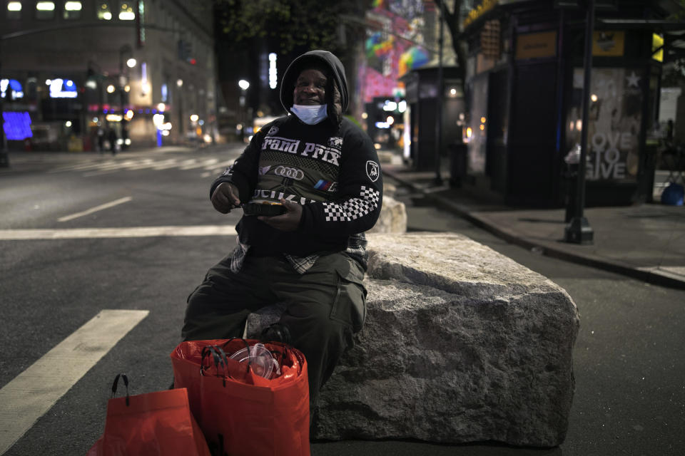 Herold Butler, 78, sits on a boulder with his belongings by his side as he eats food prepared and donated by Taheni Mediterranean Grill in Brooklyn, in New York, on Monday, April 27, 2020. (AP Photo/Wong Maye-E)