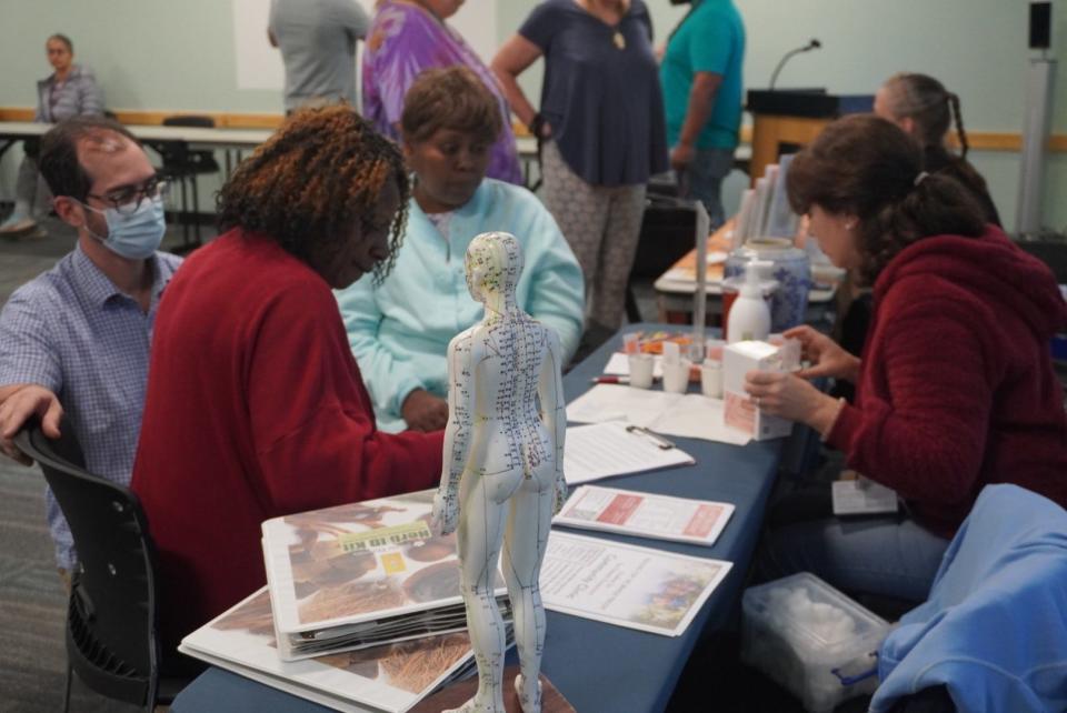 An employee of Academy for Five Element Acupuncture, right, helps attendees to her left during the Community Health and Healing Fair. Eric Abreu, far left, also assists attendees at the event held Saturday at the Library Partnership in northeast Gainesville