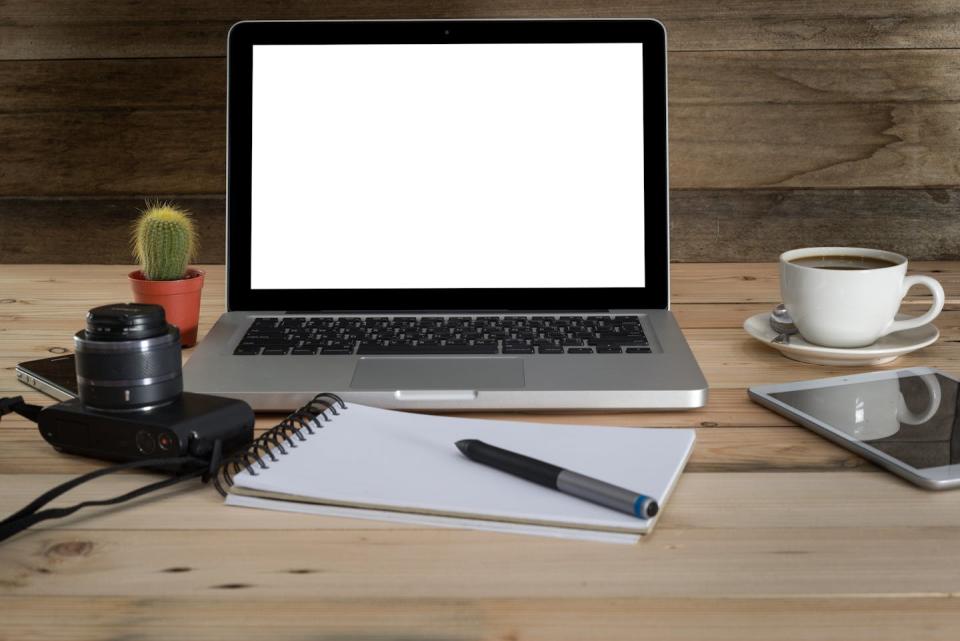 A laptop seen with camera, notebook and cactus.