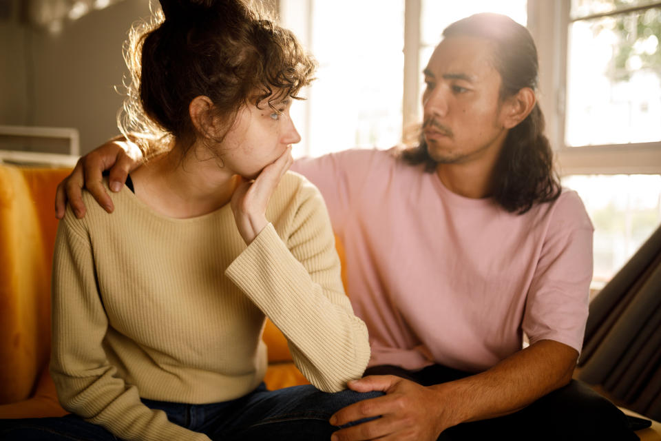 Two people sitting, one comforting the other with a supportive hand, showing concern and care